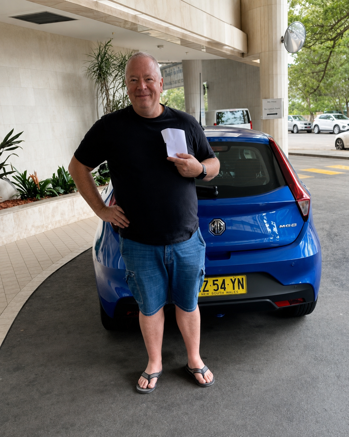 Happy CarNet renter standing beside a blue MG hatchback